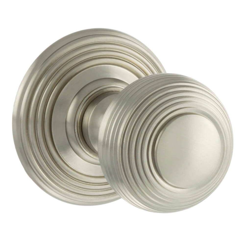 A pair of round satin nickel door knobs with a matching round backplate, featuring concentric ring detailing and a brushed metallic finish, shown on a solid white background.