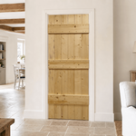 Lifestyle A light pine wood barn-style interior door with horizontal rails, shown installed in a white door frame within a bright, modern room featuring stone tile flooring and a dining area in the background.